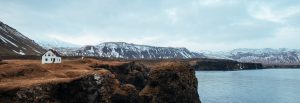 Scenic image of a house overlooking a large body of water with snow covered mountains in the background